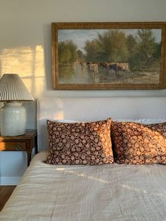 a bed with two pillows on it and a painting hanging above the headboard in a bedroom