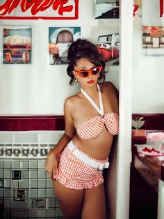 a woman in a bathing suit and sunglasses leaning against the wall with her hand on her hip