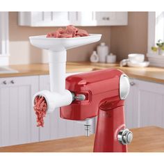 a red mixer with food in it on top of a wooden table next to white cabinets