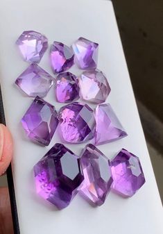 purple crystals are on a white surface and someone is holding them up to the camera