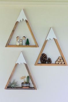 three wooden triangle shelves with pine cones and decorations on them, hanging from the wall