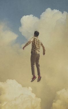 a man flying through the air on top of a cloud filled sky with his feet in the air