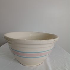 a white bowl with blue and pink stripes sitting on a tablecloth covered table cloth