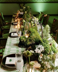 a long table is set with green and white flowers, greenery, candles and plates