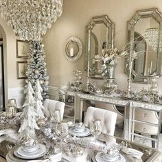 a dining room table decorated for christmas with silver and white decorations on the top, along with an ornate mirror chandelier