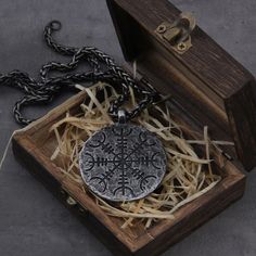 an ornate silver pendant in a wooden box on a chain, with straw around it