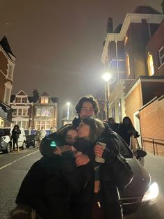 two people standing next to each other in front of a car on a city street