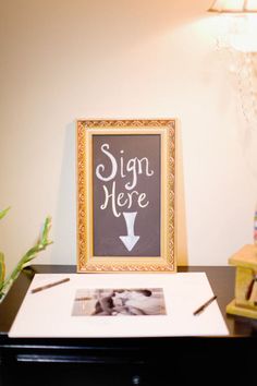 a sign that is on top of a desk next to a potted plant and lamp