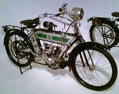 an old model motorcycle sitting on display in a museum setting with two other bikes behind it