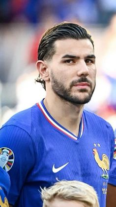 a man with long hair and beard wearing a blue soccer uniform standing next to another man