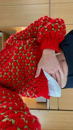 a woman wearing a red knitted scarf with green and white flowers on the edge