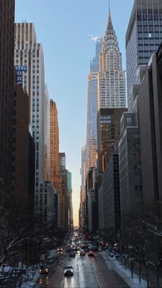 a city street filled with lots of traffic next to tall buildings and snow covered ground