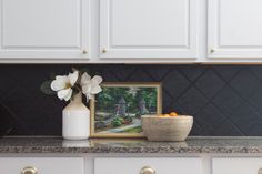 a bowl of oranges sitting on top of a counter next to a vase with flowers