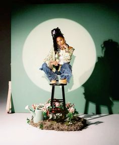 a woman sitting on top of a stool in front of a green wall