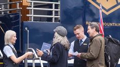 three people standing in front of a blue truck talking to each other and holding papers