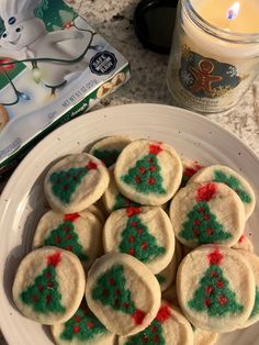 cookies decorated with green and red icing on a white plate next to a candle