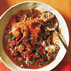 a white bowl filled with shrimp and rice on top of a red place mat next to a spoon