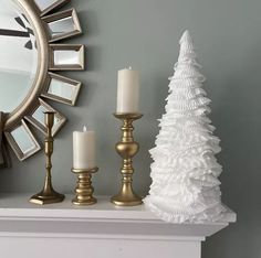 a white christmas tree sitting on top of a mantle next to two candles and a mirror