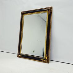 a mirror sitting on top of a white floor next to a black and gold frame