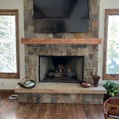 a flat screen tv mounted above a stone fireplace in a living room with hardwood floors