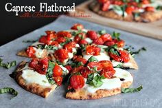 a pizza topped with tomatoes and cheese on top of a cutting board next to another pizza