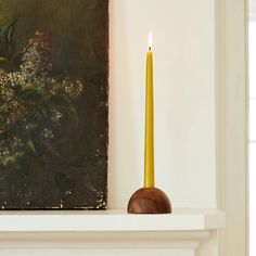 a yellow candle sitting on top of a white mantle next to a painting and vase