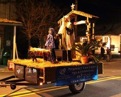 a nativity scene is being carried down the street by a horse drawn wagon with hay on it