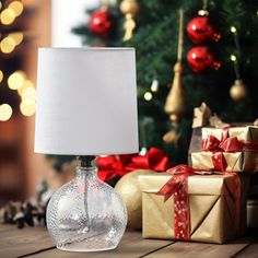 a christmas tree with presents around it and a lamp on the table next to it