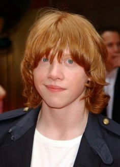 a close up of a person with red hair wearing a jacket and smiling at the camera