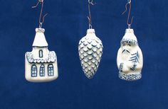 three ceramic ornaments hanging from strings on a blue background, one with a house and the other with a bird