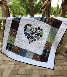 a quilted heart is displayed on a porch railing with trees in the back ground