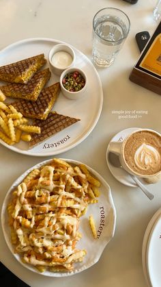 two plates with waffles and french fries on top of a table next to a cup of cappuccino