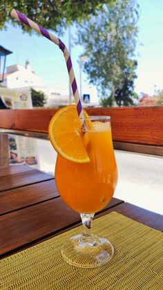 an orange drink with a striped straw in a glass on a wooden table outside,