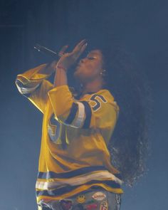 a woman singing into a microphone while holding her hands up in the air on stage