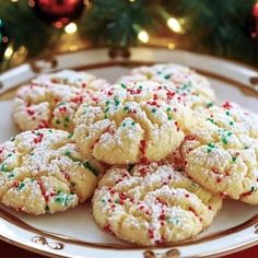 a white plate topped with cookies covered in sprinkles next to a christmas tree