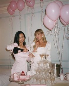 two women standing next to each other at a table with pink balloons and desserts