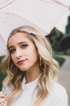 a woman with blonde hair holding an umbrella over her head and looking at the camera