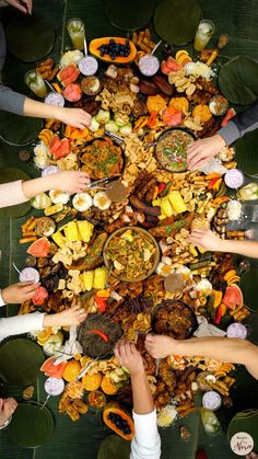 many people are holding their hands over a table full of food