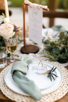 a place setting with white plates and green napkins on top of it, along with greenery