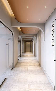 an empty hallway with white walls and lights on the ceiling is lit by recessed lighting