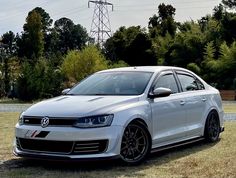 a white car parked on top of a grass covered field next to trees and power lines