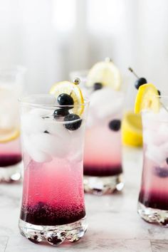 three glasses filled with different colored liquid and lemon slices on top of a marble table