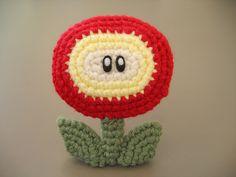 a crocheted red and yellow flower with eyes on it's head sitting on top of a table