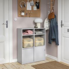 a white shelf with baskets and towels on it next to a door in a pink room