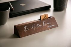 a wooden business card holder sitting on top of a table next to a laptop computer