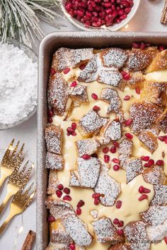 a pan filled with dessert and topped with powdered sugar, pomegranates