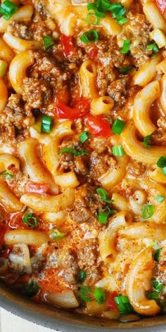 a skillet filled with pasta and meat covered in sauce, green onions and parsley