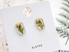 a pair of earrings with flowers on them sitting on top of a white card board