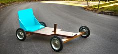 a small wooden cart with wheels and blue seat sitting on the side of a road