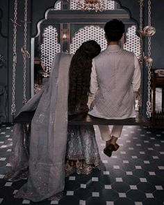 a man and woman sitting on a bench in front of an ornate room with chandelier